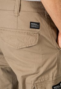 Beige Cargo-Shorts aus strukturiertem Stoff mit einem dezenten Karomuster. Mit einer Gesäßtasche, die ein schwarzes Etikett und kontrastierende Nähte aufweist.