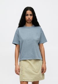 Krótki rękaw, oversized T-shirt w jasnoniebieskim kolorze z bawełny, z okrągłym dekoltem i luźnym krojem, w połączeniu z beżową spódnicą.