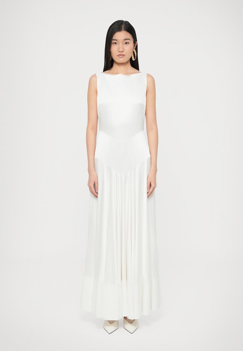 Ilga balta suknelė su prigludusiu viršumi ir plačia, plisuota, laisvai krentančia sijono dalimi. Lygus audinys su subtiliu blizgesiu, širdies formos iškirpte ir be rankovių.