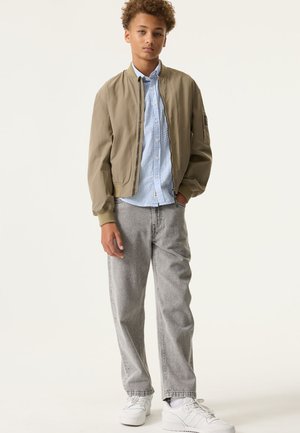 Chaqueta bomber verde oliva, camisa abotonada a rayas azul claro, vaqueros grises y zapatillas blancas. Corte casual con puños y cinturilla de canalé.