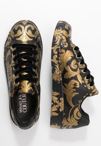 Černé tenisky s lesklým povrchem, zdobené zlatým barokním vzorem. Zaoblená špička, černé tkaničky s texturou a zlaté průchodky.