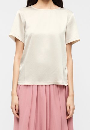 Vrouw draagt een effen off-white T-shirt met korte mouwen, gecombineerd met een hoge taille, geplooide, pastelroze rok.