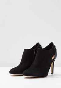 Des bottines en suède noir présentant un bout pointu, une fermeture éclair sur le côté, un design de talon découpé et un talon aiguille fin. Doublure intérieure lisse.