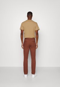 Brown trousers with a slim fit, paired with a beige short-sleeve shirt, viewed from the back against a plain white background.