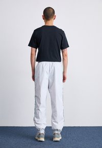 Černé tričko s krátkým rukávem, bílé zúžené kalhoty s elastickými manžetami a zelenými bočními pruhy, doplněné šedými teniskami. Jednoduchý a funkční design.