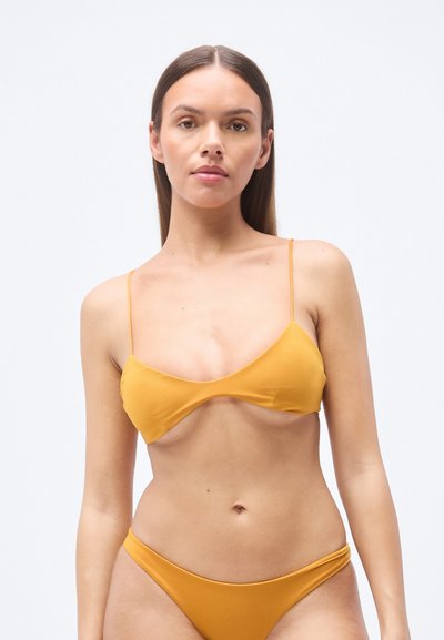 Ensemble bikini jaune moutarde comprenant un haut bralette triangulaire à fines bretelles et un bas assorti taille basse, texture lisse, design minimaliste.