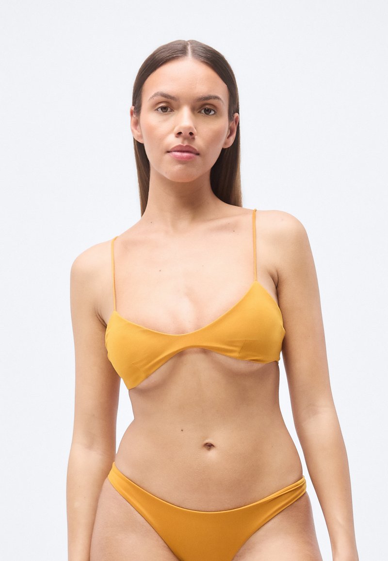 Ensemble bikini jaune moutarde comprenant un haut bralette triangulaire à fines bretelles et un bas assorti taille basse, texture lisse, design minimaliste.