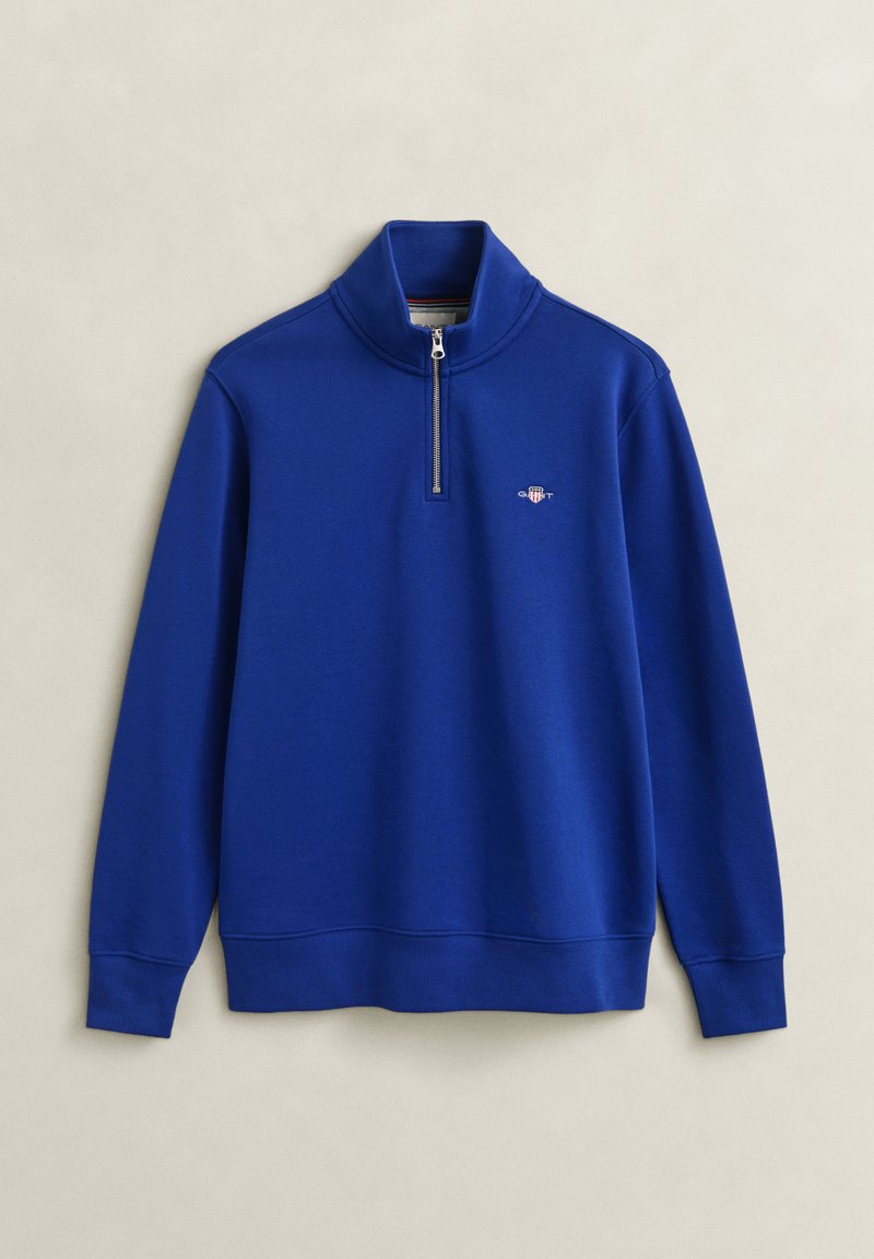 Blue long-sleeve pullover with quarter-zip collar and small embroidered logo on the left chest, laid flat on a light background.