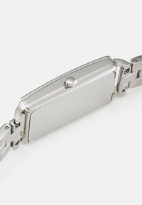 Stålarmbandsur med fyrkantig boett, polerad yta och en krona. Har en länkarmband och en slät, tom baksida.