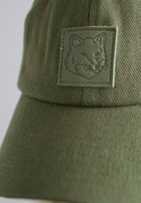 Olíva zöld sapka texturált anyagból; elülső részén kiemelkedő, dombornyomott farkasos címer található.