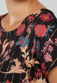 Květinový top s krátkým rukávem v černé barvě s živými růžovými, modrými a zlatými vzory, kulatým výstřihem a zlatými akcentními linkami.