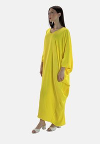 Żół dress oversize z dekoltem w serek i rękawami o długości 3/4. Wykonany z lekkiego materiału, ma luźny krój oraz kieszenie po bokach.