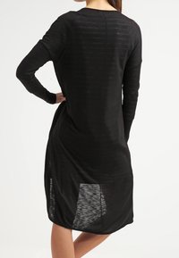 Sort langærmet kjole med afslappet pasform, der har en scoop-neck og gennemsigtige sidepaneler på kanten. Glat, let stof.