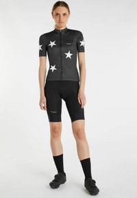 Korte mouw fietsjersey in het zwart met een wit sterrenpatroon, gecombineerd met zwarte shorts. Gemaakt van rekbaar materiaal voor comfort en flexibiliteit.