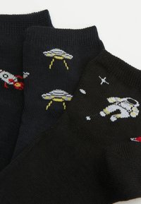 Tre paia di calzini neri con design a tema spaziale: razzi, UFO e un astronauta, ciascuno con modelli a maglia colorati.
