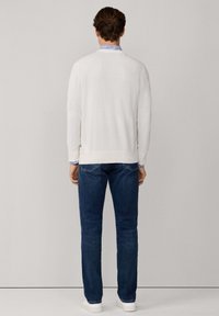 Witte gebreide trui, marineblauwe jeans en witte sneakers. De trui heeft lange mouwen en een ronde halslijn, met een gladde textuur.