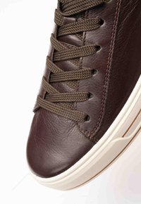 Close-up of brown leather sneaker with brown woven laces and white rubber sole with textured grip.