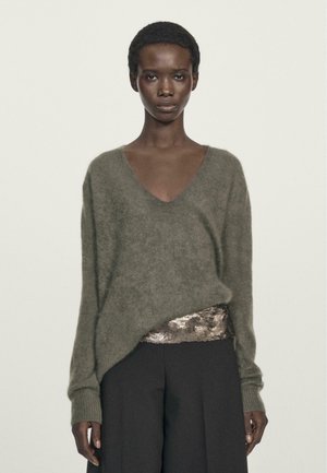 Olive green v-neck knit sweater with a soft texture, featuring long sleeves and a loose fit, paired with dark wide-leg pants and sequin detail.