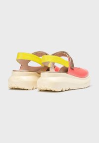 Sandalias deportivas con un upper en color coral, correa amarilla y suela gruesa en crema. Presenta un talón texturizado para un mejor agarre y una forma redondeada.