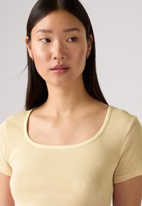 Απαλό κίτρινο ριμπ μπλουζάκι με στρογγυλή λαιμόκοψη και κοντά μανίκια, με εφαρμοστή γραμμή και λεία υφή υφάσματος.