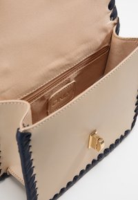 Borsa a tracolla sintetica beige con accenti intrecciati navy. Presenta un gancio dorato e una tasca interna con zip, con una morbida fodera in tessuto.