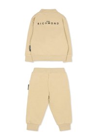 Ensemble de survêtement en coton beige avec une veste à col et un pantalon à taille élastique. Présente "JOHN RICHMOND" imprimé au dos en lettres foncées.