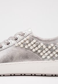 Srebrny sneaker z satynowymi sznurówkami, ozdobiony rzędami małych pereł i przezroczystych cyrkonii wzdłuż boku.