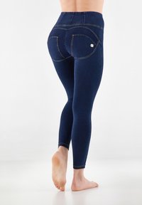 Leggings navy a vita alta con una texture liscia. Presentano cuciture decorative e due tasche posteriori. Materiale elastico per una vestibilità aderente.