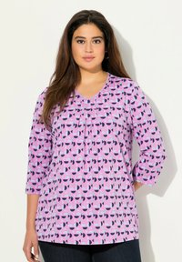Polo mit V-Ausschnitt aus lila Stoff mit einem geometrischen Muster aus pinken, blauen und marineblauen Formen; Dreiviertelärmel und lockerer Schnitt.
