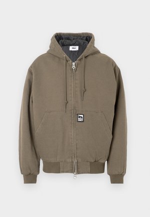 Jachetă cu glugă din bumbac verde măsliniu, cu închidere cu fermoar, prevăzută cu un buzunar tip cangur și o mică etichetă cu logo-ul brandului în față.