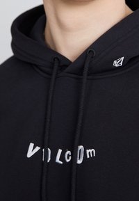 Felpa nera con cappuccio e cordino, con il logo "VOLCOM" ricamato in bianco. Tessuto morbido e scollatura distintiva.