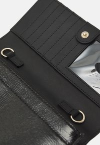 Svart läderplånbok med strukturerad yta, dragkedjestängning, kortfack, genomskinligt ID-fönster och guldfärgade detaljer.