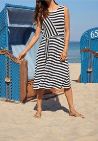 Striped sleeveless dress in navy and white, featuring a wrap-style silhouette and a tied waist. Worn with strappy flat sandals on sand.