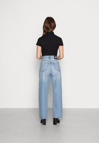 Černý žebrovaný top s krátkým rukávem v kombinaci se světle modrými širokými džínami. Džíny mají vysoký pas a štítek na zadním pásu. Černé boty na podpatku.