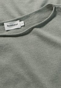 Hellgrauer Strickpullover mit rundem Ausschnitt. Trägt ein Etikett mit der Aufschrift "hessnatur", das Größe S anzeigt. Weiche Textur und glatte Oberfläche.