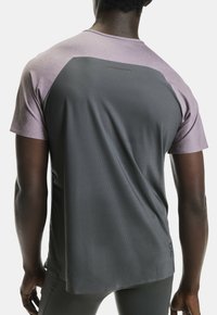 Lyhythihainen urheilupaita, jossa on sileä tummanharmaa vartalo ja vaaleanvioletit olkapääpaneelit, valmistettu hengittävästä, teksturoidusta materiaalista.