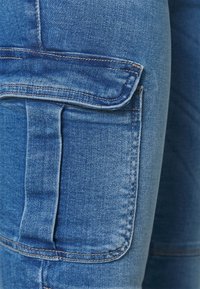 Blå denim cargo byxor med en sidficka, tillverkade av ett robust tyg, med sydda sömmar och en slät, något strukturerad yta.