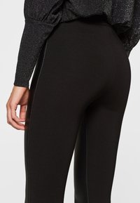 Svarta leggings med ett slätt, stretchigt material, som har en smal passform och kontrasterande sid sömmar. Framhett av subtil lyster från tygtexturen.
