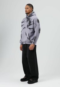 Grijze tie-dye hoodie met een zak aan de voorkant, een ontspannen pasvorm en een verstelbare trekkoord. Gecombineerd met zwarte wijd uitlopende broek en zwarte plateauzolen.