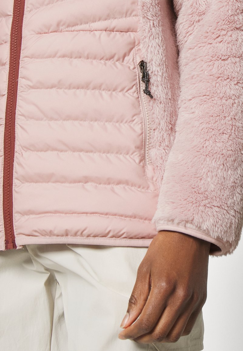 Helles rosa Jacket mit ge quilteter Textur am Körper, flauschigen Ärmeln, einer seitlichen Reißverschlusstasche und einem kontrastierenden bordeauxroten Reißverschluss.