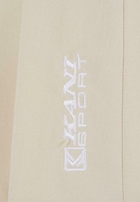 Logo blanc "KAMAZ SPORT" brodé sur un tissu beige avec une couture visible le long du bord droit.