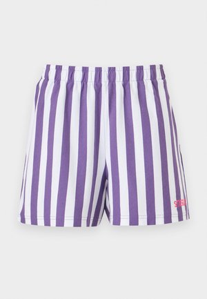 Osoba nosiaca fialové veľké tričko s veľkým modrým kvetinovým vzorom, fialové a biele pruhované šortky, biele ponožky a béžové tenisky.