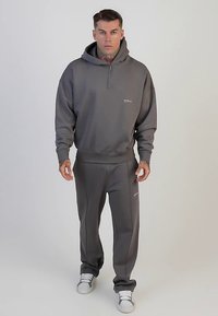 Grijze hoodie met halve ritssluiting en logo, gecombineerd met bijpassende joggingbroek met naden. Gladde stof en sportieve pasvorm.