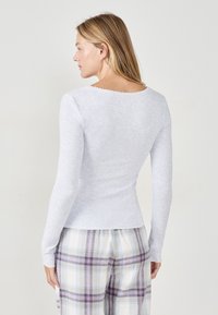 Maglietta a maniche lunghe grigia chiara con silhouette aderente, texture a coste e scollatura a onde, abbinata a pantaloni del pigiama a quadri.