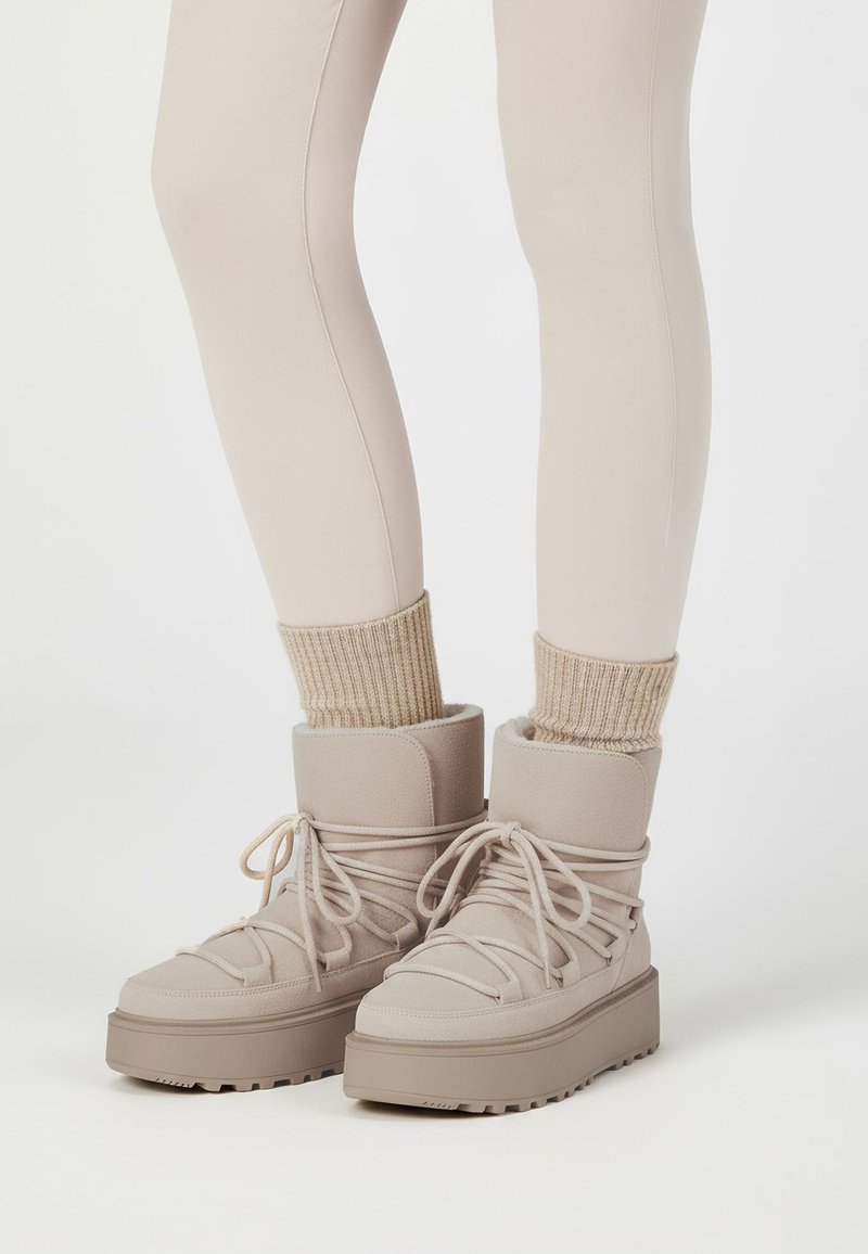 Beige Knöchelstiefel aus einem strukturierten Material, mit dicken Sohlen und Schnürdesign. Kombiniert mit gestrickten beigen Socken und figurbetonten hellen Leggings.
