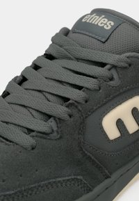 Gray sneaker made of suede and leather, featuring flat laces, a padded tongue, and a contrasting cream logo.