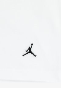 Maglietta bianca in cotone con logo Jumpman nero ricamato sul petto a sinistra. Tessuto liscio con design aderente.