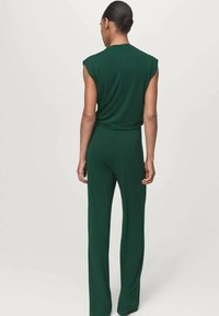 Mono verde sin mangas con cuerpo ajustado y pantalones de pierna ancha; tejido suave con detalles mínimos; la vista trasera muestra un ligero acolchado en los hombros.