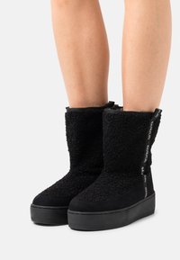 Stivali neri fino al polpaccio realizzati in un materiale texturizzato e morbido, con una suola resistente, accentuati da un'etichetta in tessuto con logo sul retro.