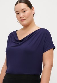 Blusa drapeada azul marino en una suave tela de jersey, con mangas cortas y escote de pico, combinada con una parte inferior negra.